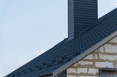 Çağdaş bir evin yeni tamamlanmış metal çatısının detaylı bir görüntüsü, bacayı ve gökyüzüne karşı düz çizgileri vurguluyor..