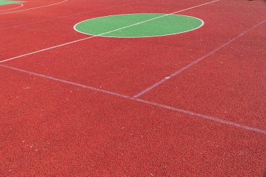 Canlı kırmızı spor yüzeyi, açık mavi gökyüzü altında çeşitli açık hava aktiviteleri için ideal büyük yeşil daireler içerir..