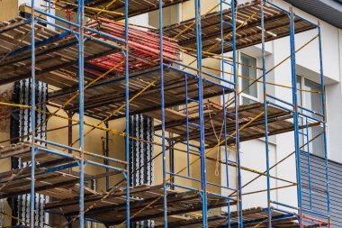 İşçiler inşaat çalışmaları için güvenlik ve ulaşılabilirlik sağlarken yenileme görevleri için bir binanın etrafına iskele hazırlıyorlar..