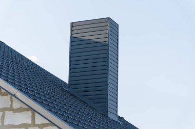 Parlak mavi gökyüzüne karşı yenilikçi tasarım elementlerini vurgulayan zarif, modern bir baca dokulu bir çatıdan yükselir..