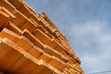 Kereste yığınları gökyüzüne doğru açık mavi bir zemin üzerine uzanır, doğal ahşap ve işçiliğin güzelliğini gözler önüne serer..