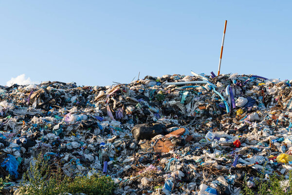 Под голубым небом выделяется огромная куча мусора, загроможденного пластиком, подчеркивая основные проблемы обращения с отходами..
