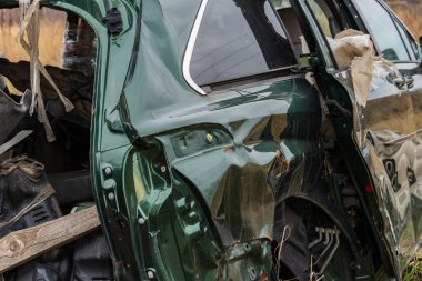 Terk edilmiş bir otomobil, bir tarlada duruyor. Geçmişteki bir kazanın verdiği hasarı gösteriyor. Çevresini çevreleyen doğal manzaraya karşı yan yana..