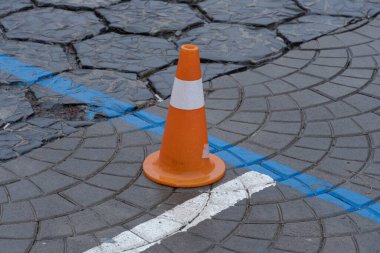 Kentte potansiyel bir inşaat alanı veya yasak bölge anlamına gelen mavi çizgilerin yer aldığı yıpranmış kaldırımın yanında duran bir trafik konisi.