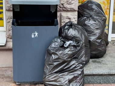 Öğleden sonra şehir caddesinde bir çöp kutusunun yanına yığılmış çok sayıda siyah çöp torbası, şehir atığı yönetimi belirtileri gösteriyor..