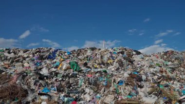 Plastik atıklar ve organik malzemelerle dolup taşan büyük bir çöp sahasını görmek, atık yönetimi ve kirlilik etkilerinin zorluklarını vurgulamak.