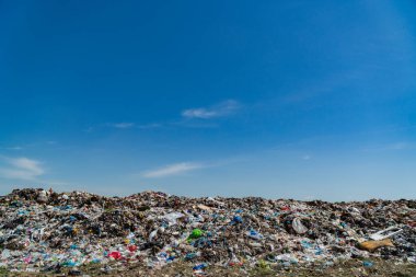 Parlak mavi gökyüzü altında çöp sahaları, plastik atıkları ve enkazı gözler önüne sererek, kirlilik sorunlarını vurguluyor.