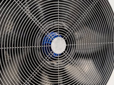 Sıcak bir ortamda verimli hava akımı için tasarlanmış spiral bıçaklarını ve merkezini sergileyen bir metal yelpazesinin ayrıntılı perspektifi..