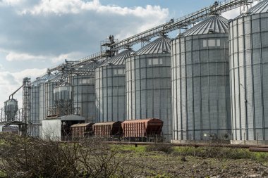 Büyük metal silolar, hasat edilen tahılları saklarken hasat edilen tahılları, ekinleri pazara taşımak için yakınlarda bekliyorlar..