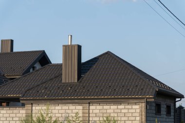 İki çağdaş ev, modern mimariyi vurgulayan açık mavi gökyüzü altında metal aksanlı ve tavan pencereli koyu fayanslı çatı sergiliyor..