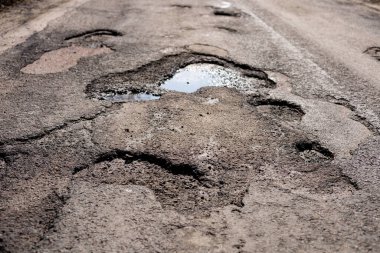 Hasarlı bir otoyol su dolu büyük çukurlar gösteriyor, sürücüler için tehlike arz ediyor ve onarımlar için acil dikkat gerektiriyor.