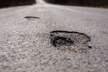 Karayolundaki çatlak asfalt araçlar için tehlike arz ediyor ve karayolu güvenliği ve trafiğinin pürüzsüz olması için acil onarım gereğini vurguluyor.