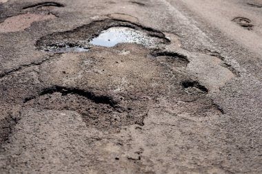 Karayolundaki çatlak ve kırık asfalt büyük çukurlar gösteriyor, araçlar için tehlike arz ediyor ve güvenliği sağlamak için acil onarım gerektiriyor.