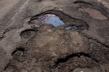 Bir otoyolun asfalt yüzeyinde birkaç büyük çatlak ve çukur tehlikeli sürüş koşulları yaratır ve acil bakım gerektirir..