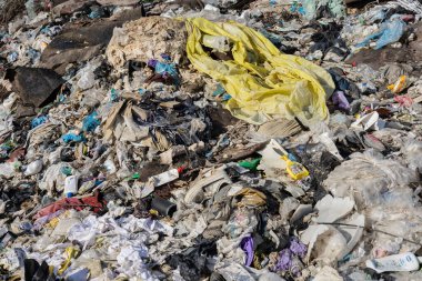 Çöpe atılmış plastik, giysi ve çöplerle dolu bir çöplük, atık yönetimi ve geri dönüşüm uygulamalarının acil ihtiyaçlarının altını çiziyor.