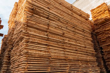 Tahta kalaslar düzgün bir şekilde kereste deposuna istiflenir. Açık bir günde, inşaat deposunun yanındaki güneş ışığını yansıtır..