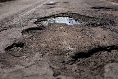 Derin çukurlar kırsal bir yolda engeller yaratıyor, baharın başlarında bulutlu bir günde yağmur suyu birikintisi oluyor..
