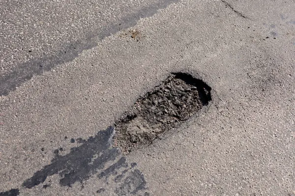 Önemli bir çukur, bir şehir caddesinin pürüzsüz yüzeyini bozar. Bu da araçların ve hava koşullarının yıprandığını gösterir..
