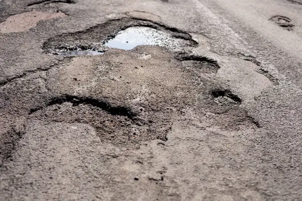 Çukurlar ve engebeli yamalar asfalt yolu kaplıyor. Depresyonlarda biriken yağmur suları yetersiz bakım ve hava etkilerini gösteriyor..