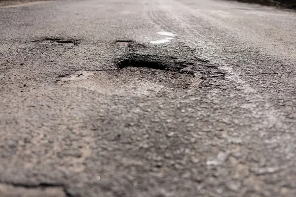 İhmal edilmiş bir sokakta derin çukurlar ve çatlamış asfalt ile önemli yol hasarı meydana getirilirken, tamirat ve bakım gereğini vurguluyor.