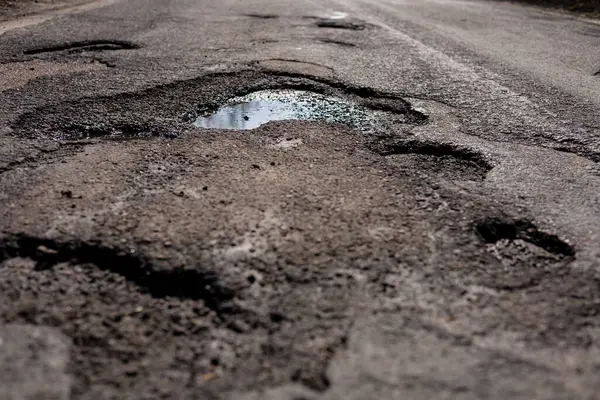 Çukurlar, şehir ortamında bulutlu bir gökyüzü altında yağmur suyu toplayarak yol yüzeyine zarar verir..