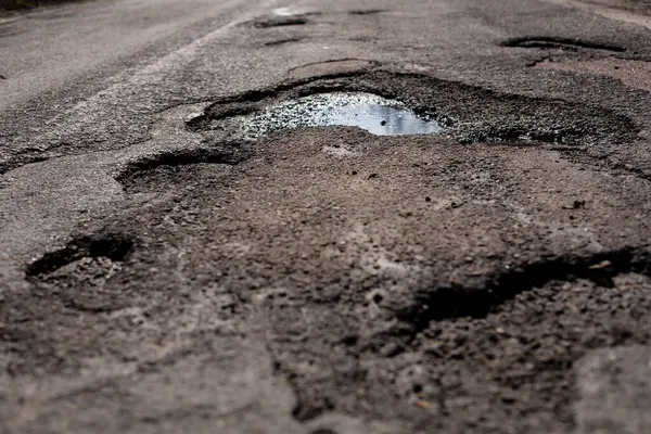 Derin çukurlar kırsal bir yolda engeller yaratıyor, baharın başlarında bulutlu bir günde yağmur suyu birikintisi oluyor..