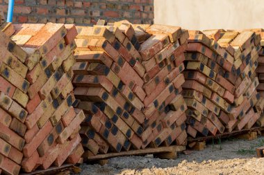 Öğlen saatlerinde parlak güneş ışığı altındaki bir inşaat alanında ahşap paletlere düzgünce dizilmiş tuğlalar..