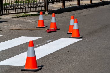 Açık gökyüzünün altında parlak renkli güvenlik konileri ve yeni boyanmış bir süpürge uzanıyor..