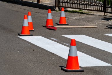 Trafik konileri, yoğun bir şehir caddesinde gündüz vakti yeni boyanmış bir yaya geçidinin etrafını sararak, yeniden boyama sırasında güvenliği sağlıyor..
