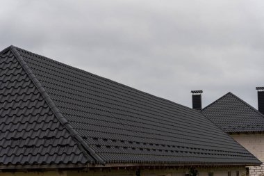 Koyu metal çatılar, bulutların muhtemel yağmura işaret ettiği bir mahalledeki evleri kaplıyor. Sahne tipik bir mimari tasarımı yakalar..