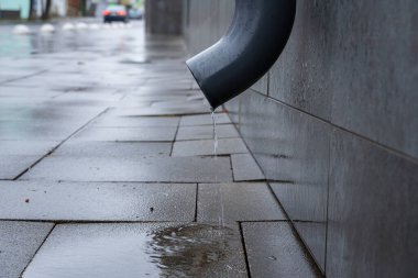 Kanalizasyon borusundan kaygan kaldırıma damlayan su, kentsel bir çevrede yağmur sonrasını gösteriyor..