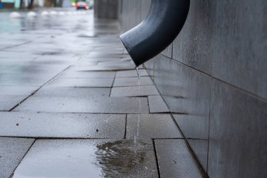 Yağmurlu bir günde, sakin bir şehir sokağındaki gri gökyüzünü yansıtan, yağmurlu bir kaldırıma damlayan su..
