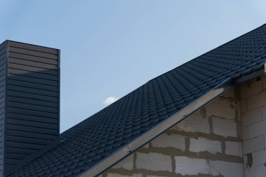 Güneşli bir günde iskan binasına yeni çatı döşeyen işçiler görülüyor. Baca gökyüzüne karşı belirgin bir şekilde yer alır..