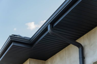 Bir çatı kenarının yakın görüntüsü ve açık mavi gökyüzüne karşı alçalma çağdaş yapı özelliklerini ve materyalleri vurgular.