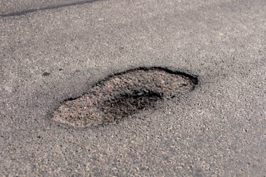 Büyük bir çukur asfalt bir yolda duruyor, trafik akışını bozuyor ve şehir çevresindeki araçlar ve yayalar için riskler oluşturuyor.