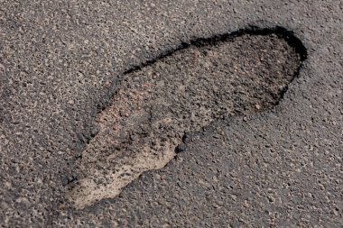 Bir asfalt caddesinde geniş bir çukur görülebilir, bölgede gezinen araçlar ve yayalar için risk arz etmektedir..