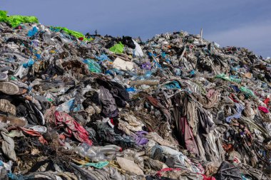 Atılan giysi, plastik ve moloz yığınları çöplüğü doldurarak, acil kirlilik ve atık yönetimi sorunlarını vurguluyor.