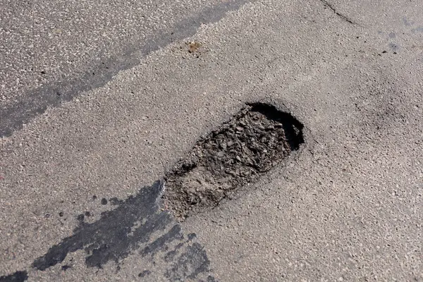 Asfalt bir yolda büyük bir çukur bulunmakta olup, gündüz vakti yerleşim yerlerinde araçlar için engeller oluşturmaktadır..