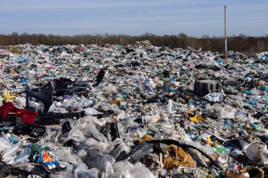 Açık mavi gökyüzü altında çeşitli plastik atık ve çöplerle dolu geniş bir alan, çevresel etki ve kirliliği vurguluyor.