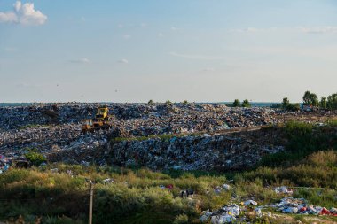 Ağır makineler çöp ve plastik atıklarla dolu bir çöp sahasının bölümlerini temizliyor ve bu alandaki kirlilik sorunlarını vurguluyor.