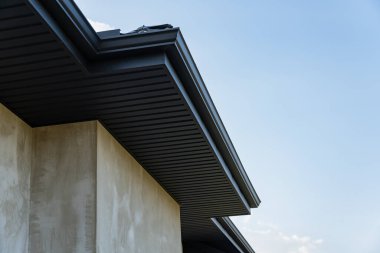 Bir binanın çatısı, parlak metalik fayanslarla ve mavi gökyüzüne uzanan pürüzsüz çizgilerle detaylı bir görünüm, inşaat çalışmalarını gösteriyor..