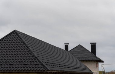 Metalik kiremitlerle kaplı çatılar, banliyöde bulutlu bir gökyüzüne karşı parlak bir tasarım sergiliyor..