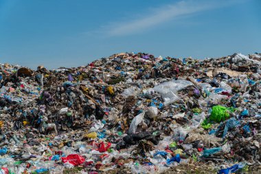 Plastik çöp ve molozlarla dolu büyük çöplük, temiz mavi gökyüzü altında çevreyi etkileyen kirlilik sorunlarını vurguluyor.