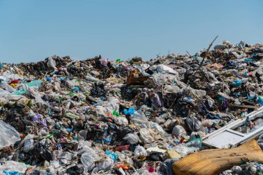 Çöp yığınları ve plastik döküntüler, sürmekte olan atık yönetimi sorunlarını ve bunun çevre üzerindeki etkisini vurgulayarak çöplüğü kaplıyor.