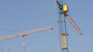 Turna makineleri, yeni bir yapı inşa etmek için açık bir gökyüzü altında ağır materyalleri kaldırarak, bir inşaat sahasında özenle çalışıyor.