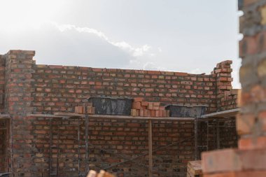 İnşaat ilerlemesi, kentsel bir ortamda parlak gökyüzü altında iskele desteğiyle tuğla duvarın yükseldiğini gösteriyor..