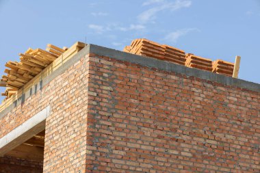 İşçiler bir tuğla bina inşa etmekle, çatıya ahşap malzemeler yığmakla meşguller..