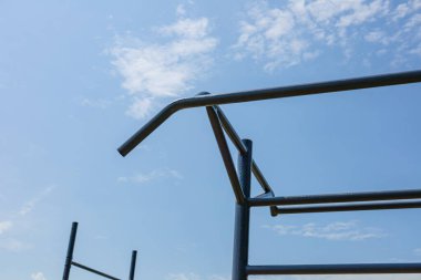 Jimnastik ekipmanları mavi gökyüzüne karşı dik duruyor, sporcuları güçlü antrenmanlara ve aktif egzersiz rutinlerine davet ediyorlar..