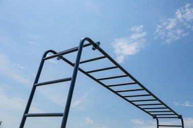 Jimnastikçi, açık mavi gökyüzü altında yatay paralel çubuklar üzerinde kuvvet eğitimine girişerek, fitness ve sağlığa olan bağlılığı vurguluyor..