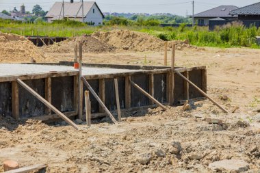 İşçiler, yeşillik ve evlerle çevrili bir inşaat alanında ahşap destekli bir vakıf kuruyorlar..